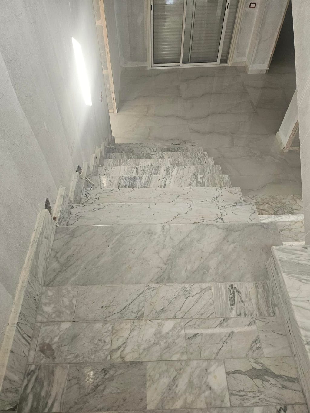 Escalier et palier habillés de marbre blanc veiné, vus depuis le haut des marches : marches et contremarches en dalles grand format, prolongées par le sol du palier.